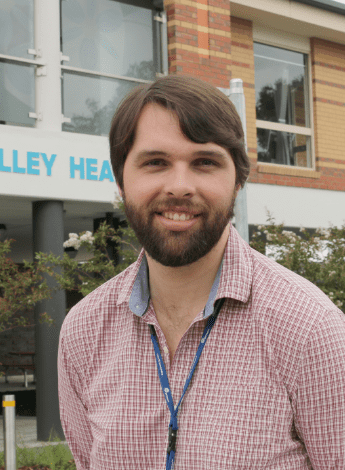 A man with a beard is standing in front of a building